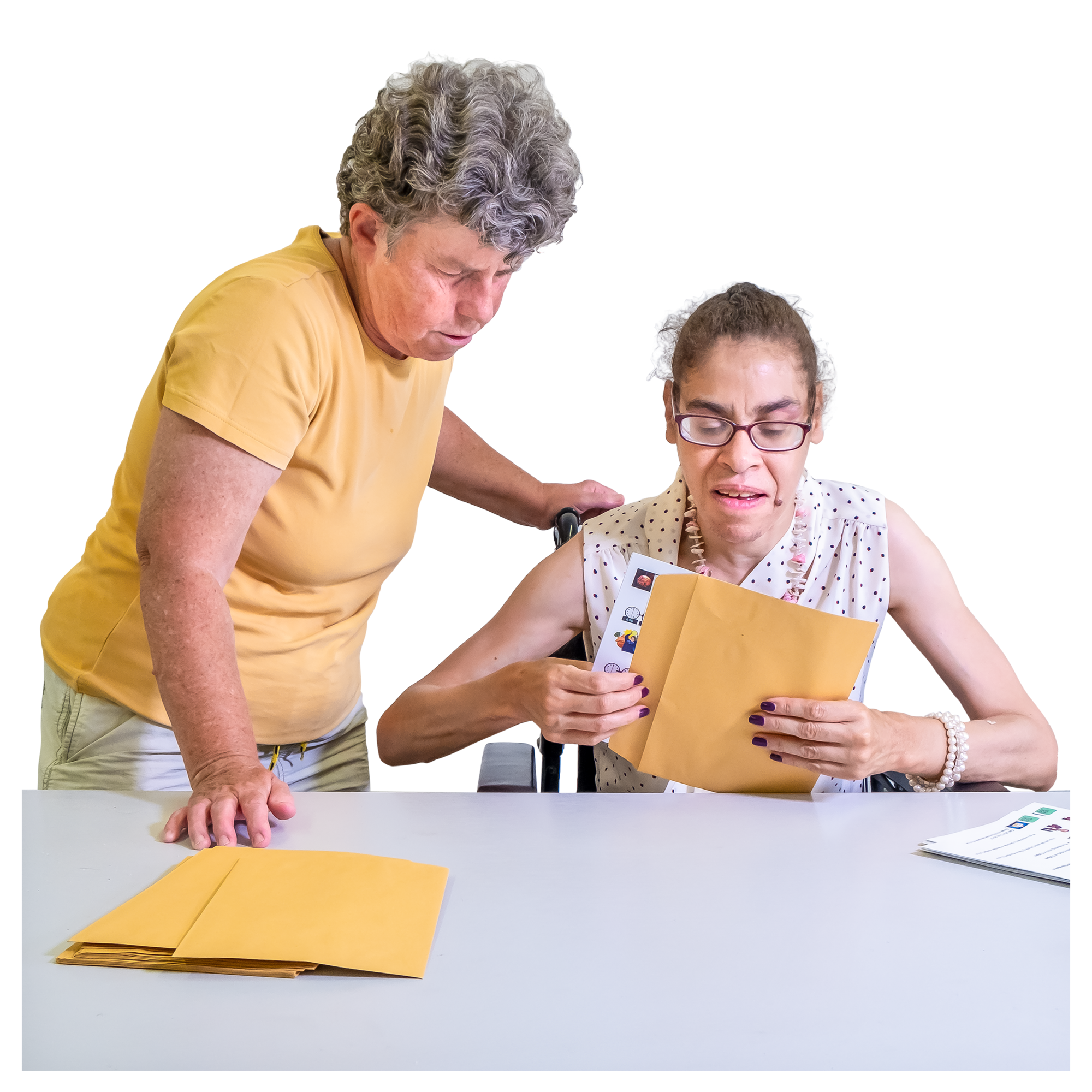 Two women, one standing and one seated. The seated woman is taking something out of a brown envelopeetter