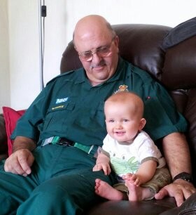 Man wearing green ambulance uniform sitting on a sofa with a baby next to him