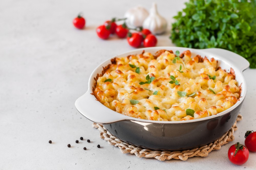 Tuna pasta bake on rustic trivet with tomatoes and garlic on the table next to it