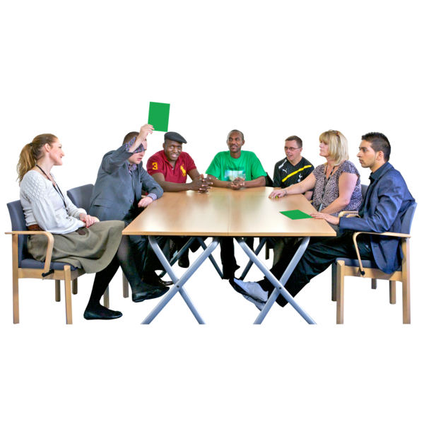 A lot pf people sitting round a meeting table. One person is holding up a green card.