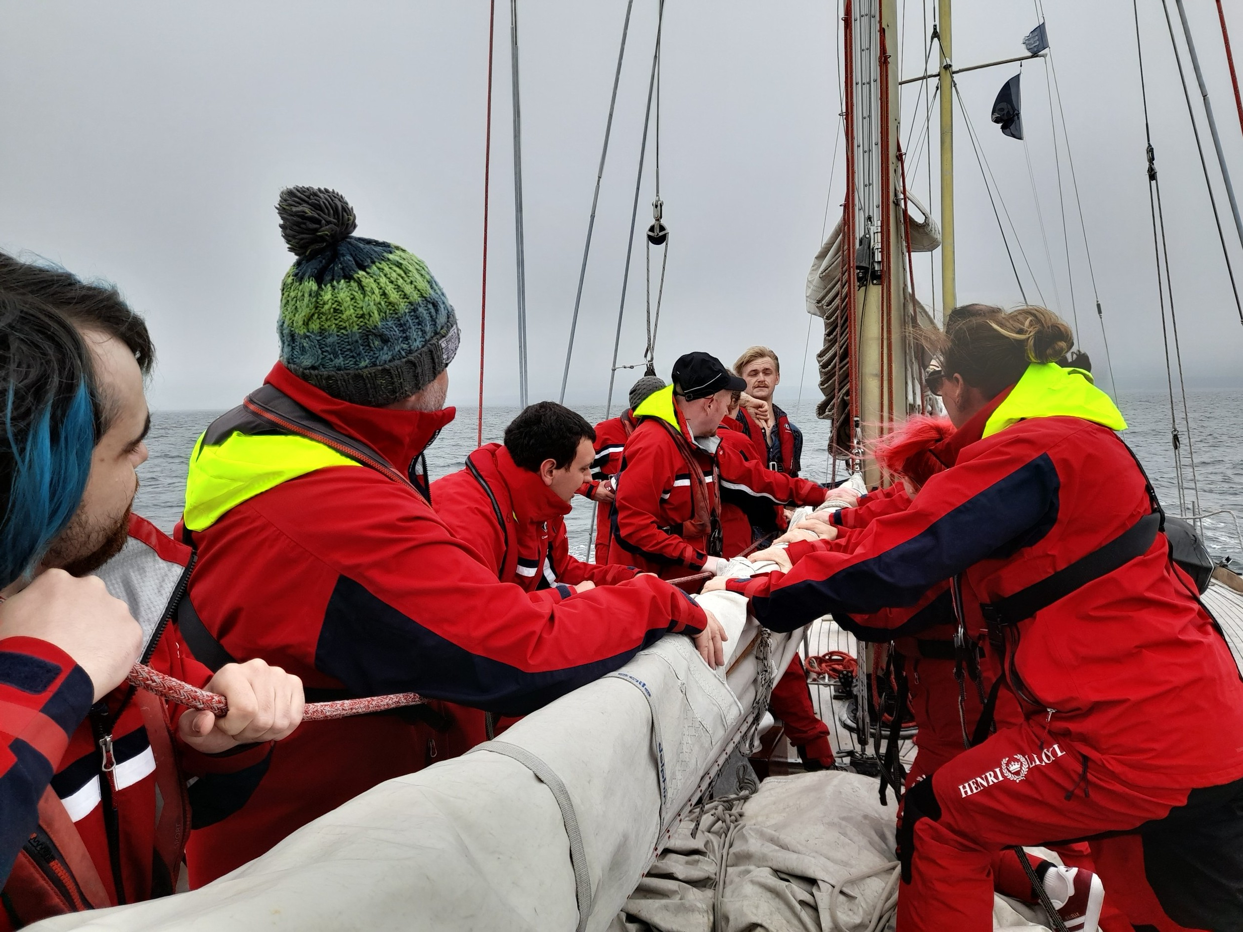 A group of people in red raincoats and warm hats attending to the sail of a boat at sea