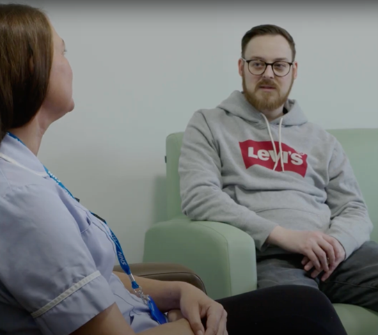 A nurse and patient sitting in chairs talking