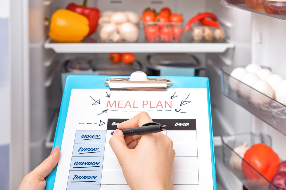 person with clip board and pen making meal plan looking in their fridge
