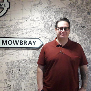 Peer support Wotker Dan briggs stands in front of a map of Sunderland and a signpost for Mowbray Ward