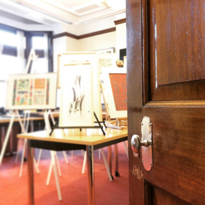 A door opening onto a room full of artworks on easels; the door is in focus, but the rest of the room is blurry.