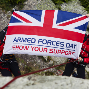 A flag being held aloft; the flag shows half of a union jack, with the words 'armed forces day, show your support' underneath