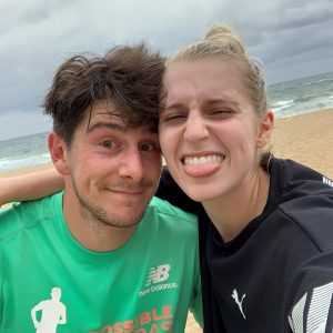Abi and Alex taking a selfie together on a windswept beach