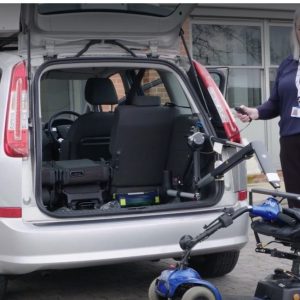 A member of the NEDM team demonstrating how to load a wheelchair into the boot of a silver hatchback car.