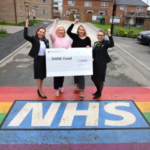 CNTW and Barratt homes staff holding a giant cheque standing on the new painted NHS rainbow at Sycamore Grove