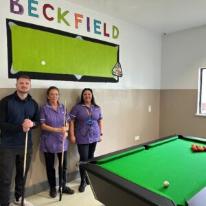 Three members of staff on Beckfield ward standing next to a new pool table