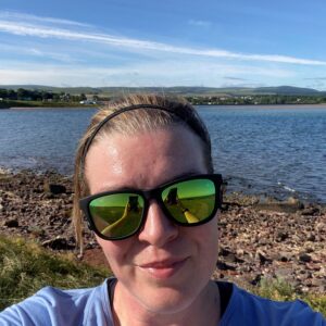 Selfie photo by a lake of a woman in sunglasses smiling at the camera