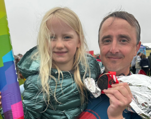 Photo of man with daughter holding up his Great North Run 2024 finisher medal