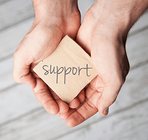 Hands holding a square block of wood with support written across the surface